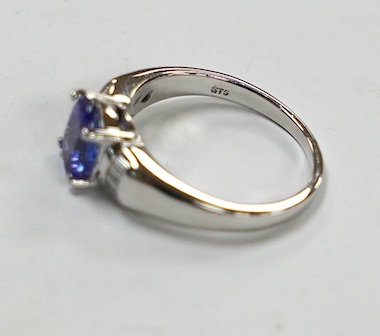 A modern 18ct gold and single stone oval cut tanzanite set ring, with baguette cut diamond cluster set shoulders, with accompanying AnchorCert report, stating the stone to weigh 1.20ct, size L, gross weight 4.1 grams. Co